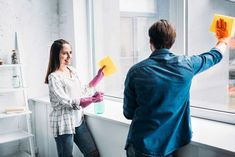 a man and woman cleaning windows with yellow sponges on the windowsill in an apartment