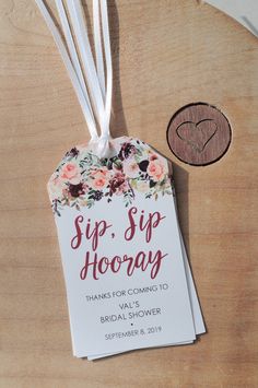 a tag that says sip sip hooray hanging from a wooden table with flowers on it