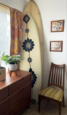 a surfboard leaning up against a wall next to a chair and window with flowers on it