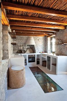 an instagramted photo of a kitchen and living room with stone walls, exposed wood beams, and flooring