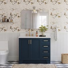 a bathroom with a blue vanity, mirror and white toilet in front of a wallpapered wall