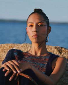 a woman sitting on top of a rock next to the ocean with her eyes closed