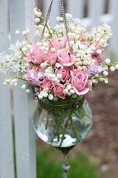 a hanging vase filled with pink roses and white baby's breath in front of a picket fence