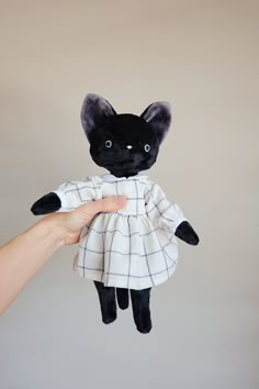 a hand holding a black cat doll with a white dress on it's body