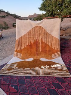 an orange and brown blanket sitting on top of a red rug next to a tree