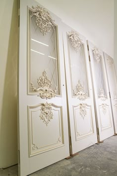 three white doors with ornate designs on them in an empty room next to a wall