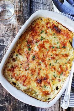 a casserole dish with cheese and parsley in it on a wooden table