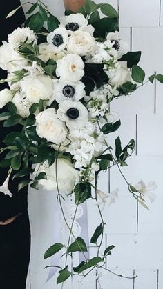 a woman holding a bouquet of white flowers and greenery in front of a wall