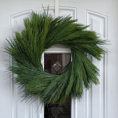 a green wreath hanging on the front door of a white house with an open window