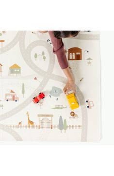 a child's hand is playing with a toy truck on a play mat that has houses and cars all over it