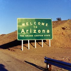 a welcome to arizona sign on the side of a road in front of a hill