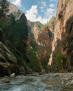 people are rafting down a river in the mountains near some rocks and trees on either side