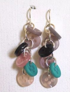 two pairs of earrings with different colored buttons hanging from the same earwires on a white surface