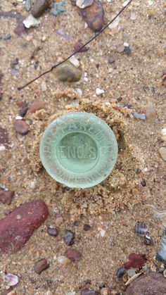 a green glass bottle sitting on top of a sandy beach next to rocks and water