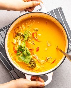 two hands holding a pot of soup with broccoli