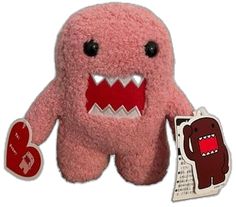 a pink stuffed animal with big teeth holding a heart shaped sticker next to it's packaging