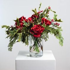 a glass vase filled with red roses and greenery