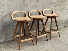 three wooden stools sitting in front of a concrete wall