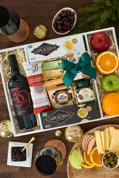 an assortment of cheeses, fruit and wine in a gift box on a table