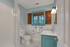 a bathroom with blue walls and white tile flooring, along with wooden shutters