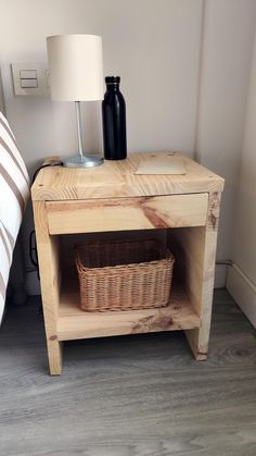 a small wooden table with a basket on it next to a lamp and a bed