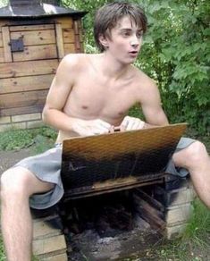 a shirtless young man sitting on top of a fire place using a laptop computer