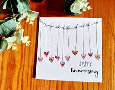 a happy anniversary card with hearts hanging from a line on a table next to flowers