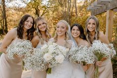 a group of women standing next to each other in front of a wooden structure holding bouquets