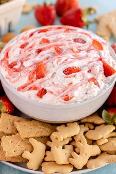 a bowl of strawberry cheese dip surrounded by crackers and strawberries on a plate