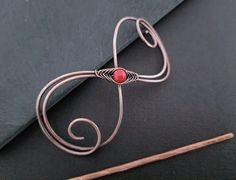 a piece of wire with a red bead on it sitting next to a pair of knitting needles