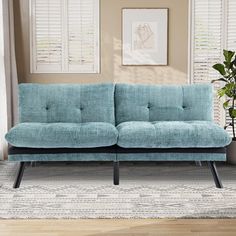 a blue couch sitting on top of a wooden floor next to a potted plant