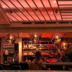 two people sitting at a bar with disco balls hanging from the ceiling and lights above them