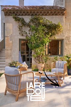 a patio with wicker furniture and potted plants on the side of the house