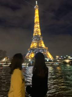 two women standing next to each other in front of the eiffel tower at night