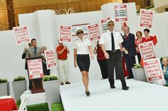 two pilots walking down the runway with signs in front of them and people standing behind them