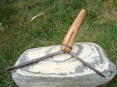 a stone with a wooden handle and two knives on it sitting in the grass next to a rock