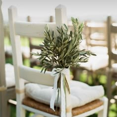 an olive branch tied to the back of a chair with white linens on it