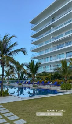 an empty swimming pool in front of a large building with palm trees and lawn chairs