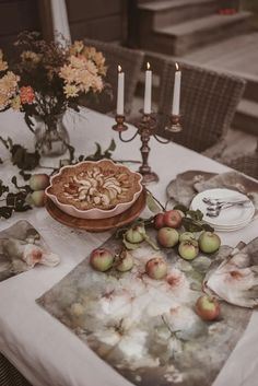 a table topped with plates and fruit next to candles on top of a wooden table