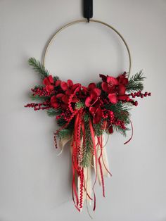 a wreath with red flowers and greenery hanging on a wall