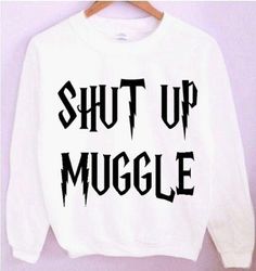 a white sweatshirt with the words shut up muggle printed on it, hanging from a wooden hanger