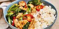 a blue bowl filled with rice, broccoli and red peppers on top of it