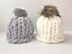 two knitted beanies with pom - poms on them sitting side by side