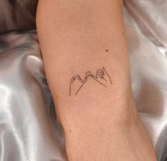 a small tattoo on the arm of a woman with mountains in the background and clouds above it