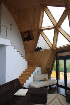 a living room filled with furniture under a wooden skylight above a staircase leading up to a second story window