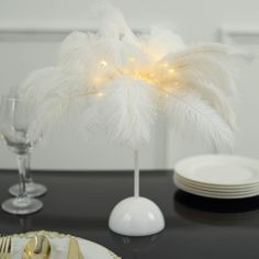 a table topped with white plates and silverware next to a vase filled with feathers