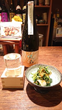 a bottle of wine sitting on top of a wooden table next to a bowl of food