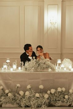 a bride and groom are sitting at a table with candles in front of their faces