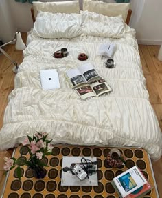 an unmade bed with magazines and flowers on the end table in front of it