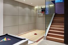 a room with a pool table, basketball hoop and stairs leading up to the upper floor